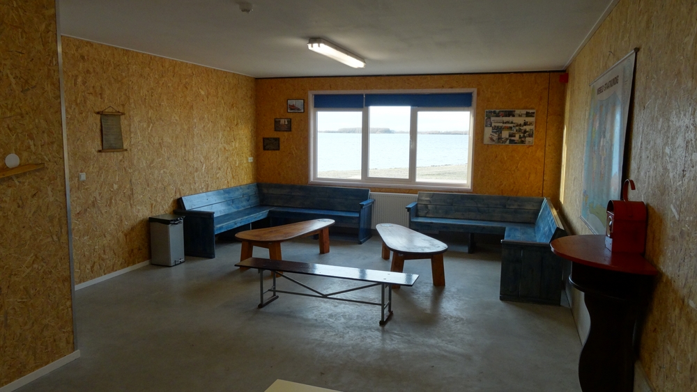 Een rustige hoek in het clubgebouw met banken bij het raam, uitkijkend over het water